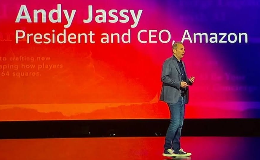 Andy Jassy on a stage. Behind him, the words "Andy Jassy President and CEO, Amazon" are visible on a big screen. 