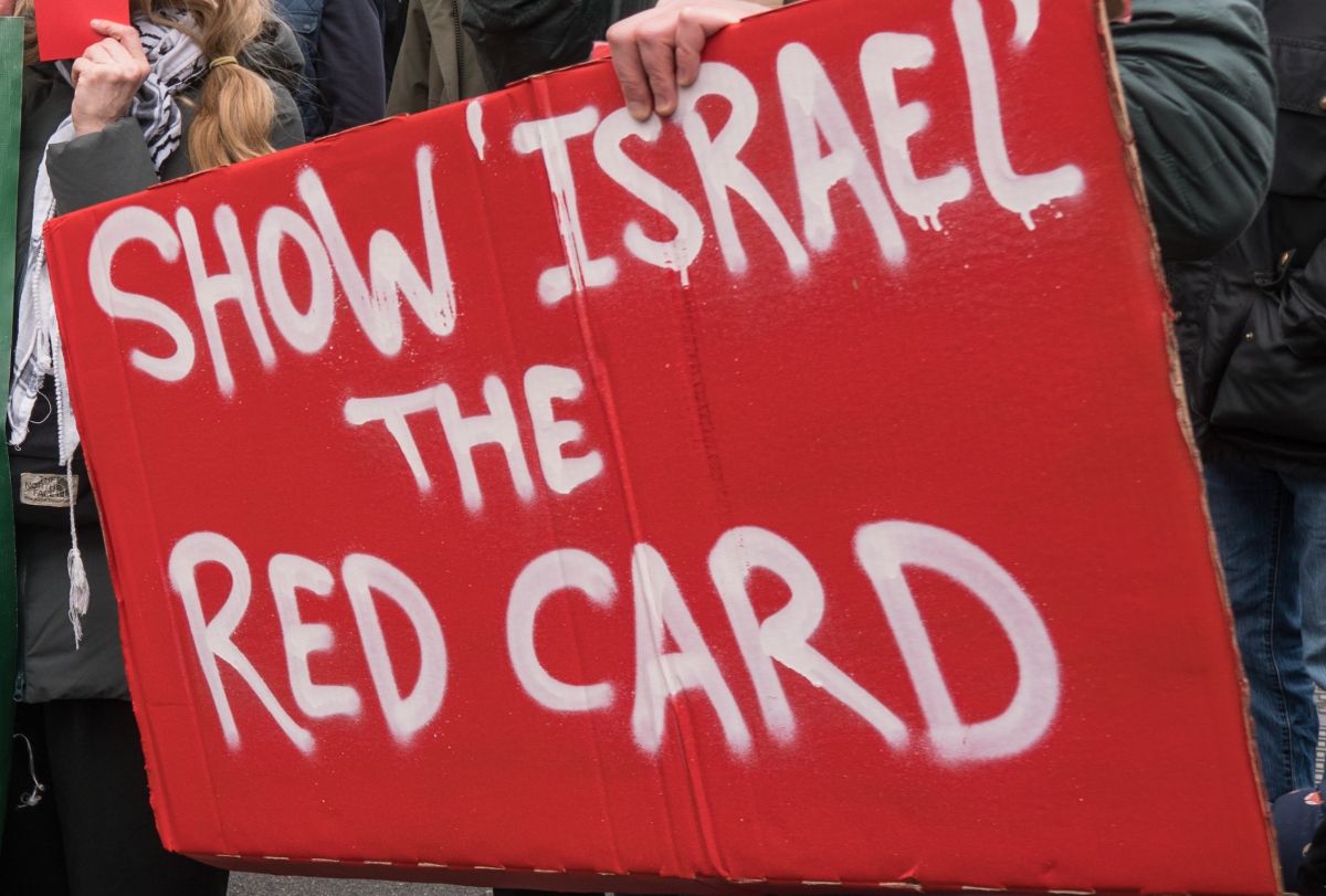 A poster being held at a protest reading show Israel the red card in red and white.