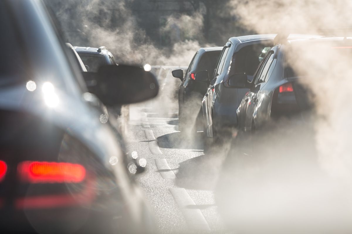 A photo of a traffic jam, lots of polluting cars lined up behind each other, exhaust fumes fill the air.